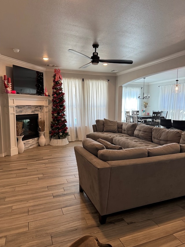 living room featuring crown molding, a stone fireplace, a textured ceiling, and light hardwood / wood-style floors