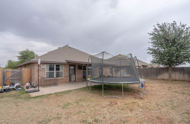 back of house featuring a trampoline, brick siding, a fenced backyard, a patio area, and a yard