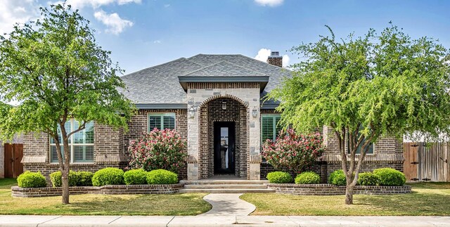view of front of property with a chimney, brick siding, fence, a shingled roof, and a front lawn