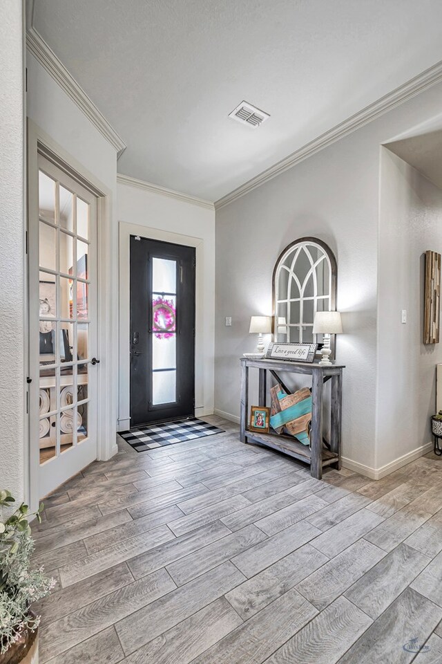 entryway featuring baseboards, visible vents, wood finished floors, and crown molding