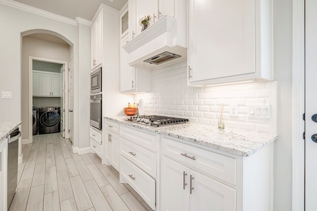 kitchen with arched walkways, decorative backsplash, independent washer and dryer, appliances with stainless steel finishes, and white cabinetry