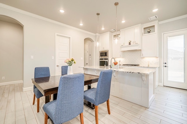 dining space with visible vents, light wood-style flooring, baseboards, ornamental molding, and arched walkways