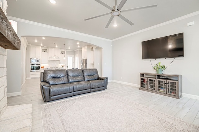 living room with ornamental molding, ceiling fan, light wood finished floors, and arched walkways