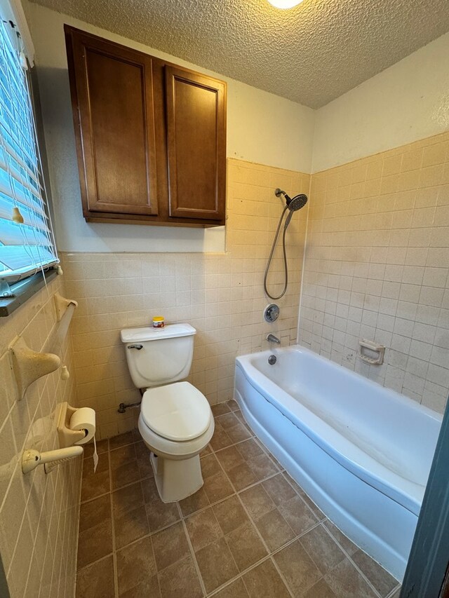 2203 40th St, Snyder, TX 79549 - full bathroom with toilet, a textured ceiling, a wainscoted wall, tile walls, and tub / shower combination