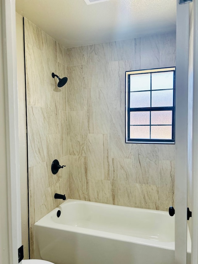 bathroom with toilet and tiled shower / bath