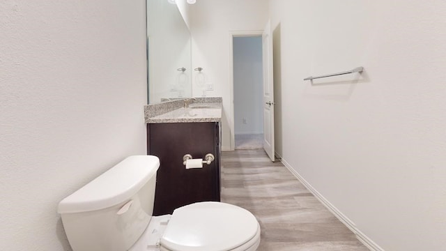 half bath with baseboards, toilet, wood finished floors, and vanity