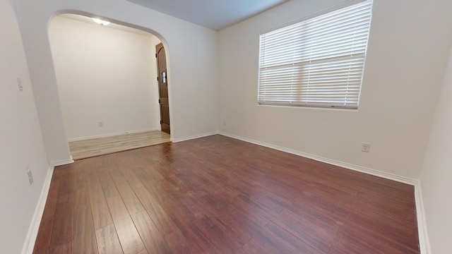 spare room with arched walkways, baseboards, and wood finished floors