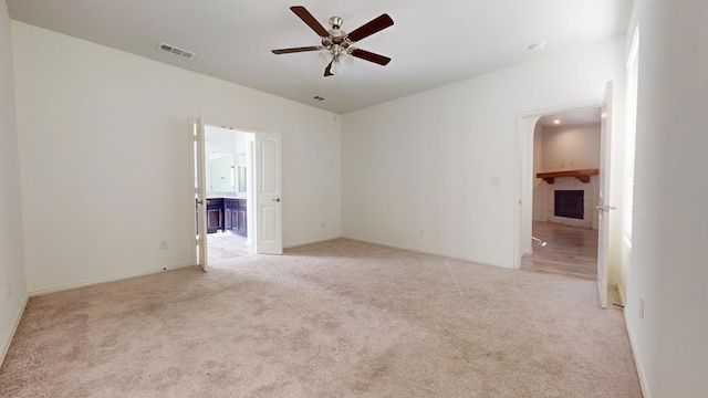 empty room featuring visible vents, baseboards, ceiling fan, light colored carpet, and a fireplace