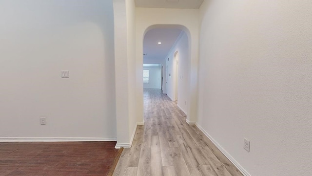 corridor featuring arched walkways, baseboards, and light wood-style floors