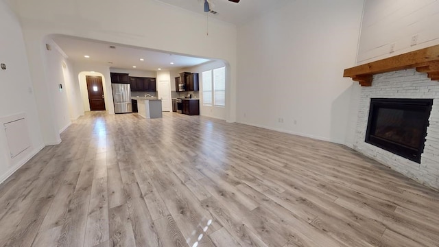 unfurnished living room with arched walkways, light wood-style flooring, a fireplace, and a ceiling fan