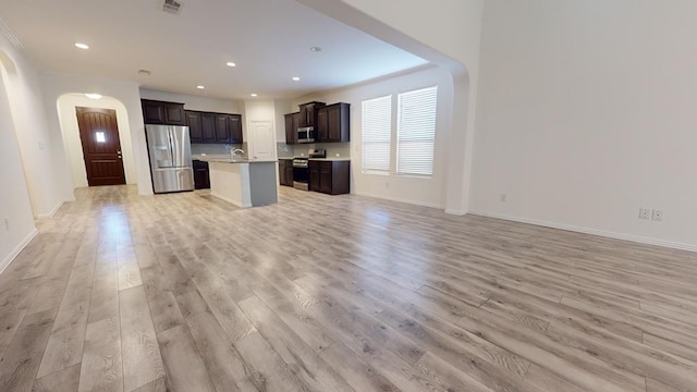 kitchen featuring light wood-style flooring, an island with sink, stainless steel appliances, light countertops, and open floor plan