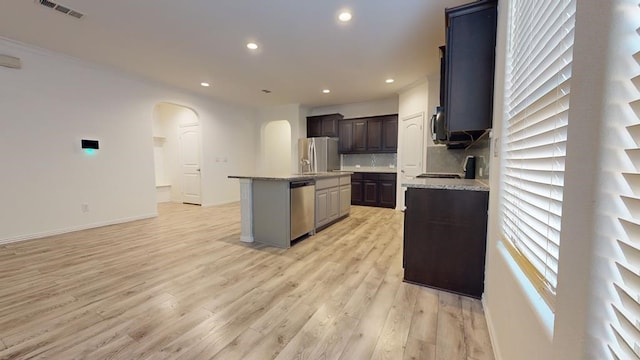 kitchen featuring visible vents, a kitchen island with sink, arched walkways, stainless steel appliances, and light wood-type flooring