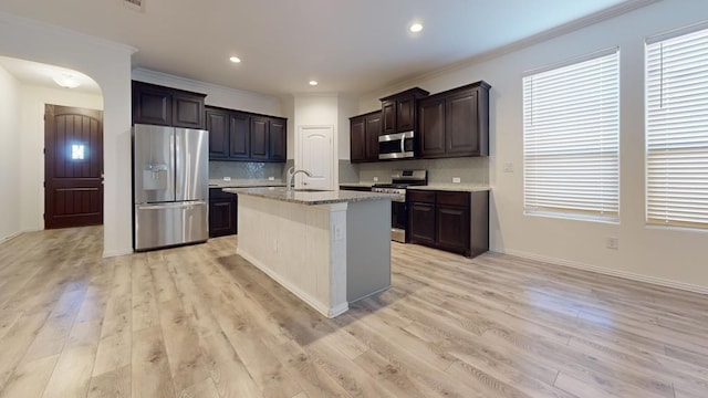 kitchen with dark brown cabinetry, decorative backsplash, light wood-style floors, stainless steel appliances, and a sink