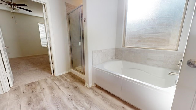 bathroom with ceiling fan, baseboards, a garden tub, a stall shower, and wood finished floors