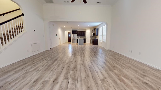 unfurnished living room with a ceiling fan, visible vents, arched walkways, and light wood finished floors