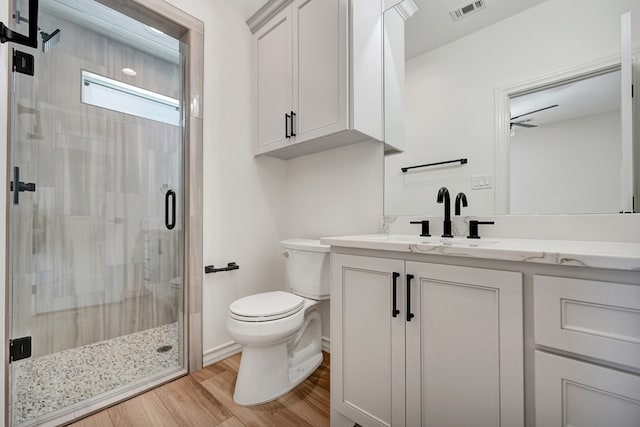 bathroom featuring visible vents, toilet, wood finished floors, vanity, and a shower stall