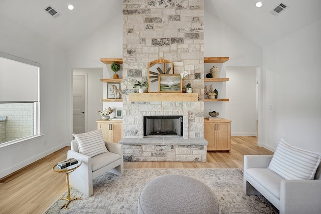 living room featuring light wood-style flooring, visible vents, high vaulted ceiling, and a stone fireplace