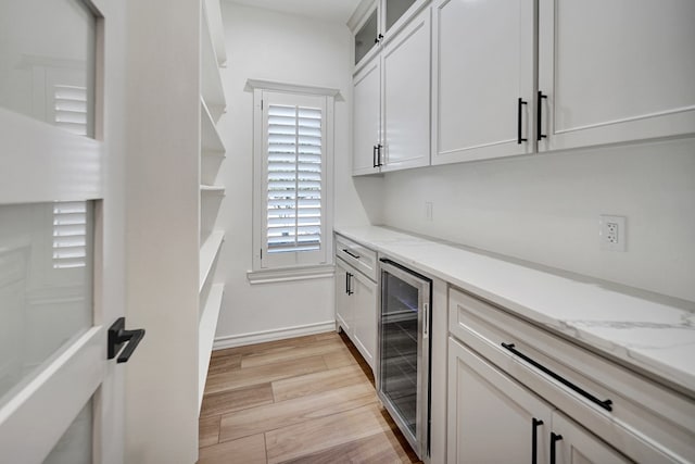 bar with beverage cooler, light wood-style flooring, and baseboards