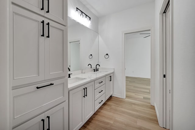 full bath featuring double vanity, wood finished floors, a sink, and baseboards