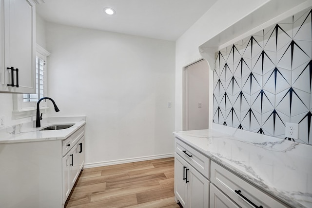 kitchen featuring light stone counters, a sink, baseboards, light wood-style floors, and white cabinets