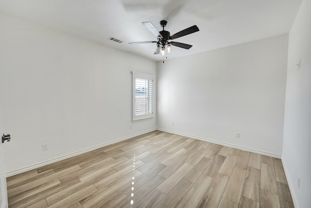 spare room with baseboards, light wood-type flooring, visible vents, and a ceiling fan