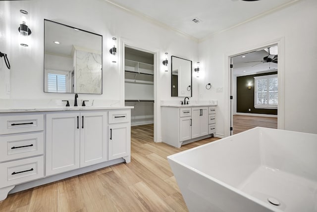 full bath featuring a walk in closet, two vanities, crown molding, and wood finished floors