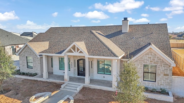 view of front of home featuring stone siding, a shingled roof, and a chimney