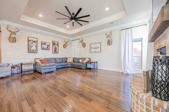 living room featuring wood finished floors, a ceiling fan, a tray ceiling, and crown molding