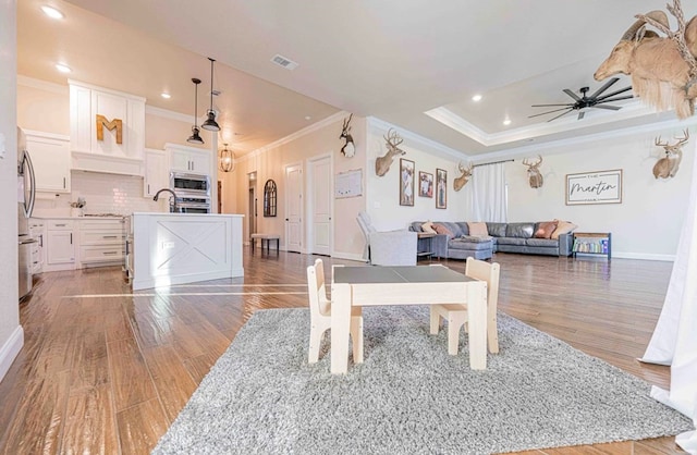 living area featuring light wood-style flooring, visible vents, ceiling fan, baseboards, and ornamental molding