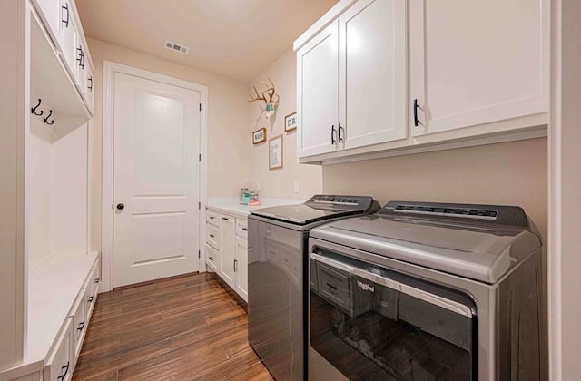 clothes washing area with dark wood finished floors, visible vents, cabinet space, and washer and clothes dryer