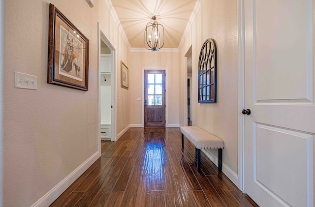 doorway with a chandelier, baseboards, crown molding, and dark wood-style floors
