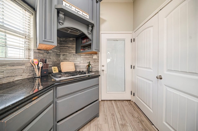 kitchen featuring gray cabinets, decorative backsplash, stainless steel gas cooktop, custom range hood, and light hardwood / wood-style flooring