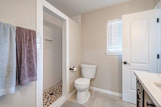bathroom featuring vanity, tile patterned floors, baseboards, toilet, and tiled shower
