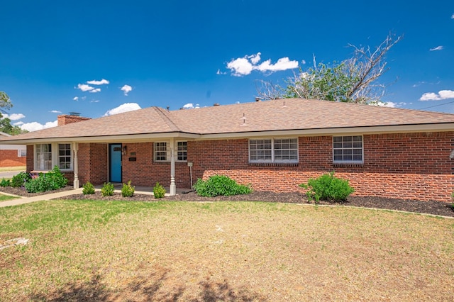 single story home featuring brick siding, a chimney, and a front yard