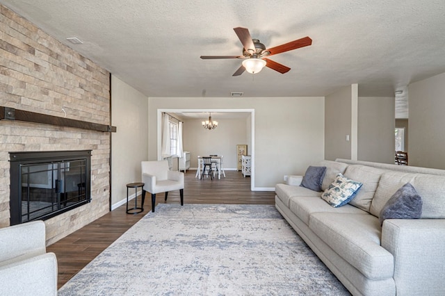 living area featuring a fireplace, a textured ceiling, ceiling fan with notable chandelier, baseboards, and dark wood-type flooring