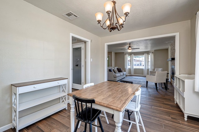 dining space with a fireplace, visible vents, ceiling fan with notable chandelier, and dark wood-type flooring