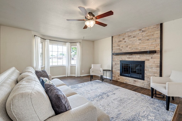 living area with baseboards, ceiling fan, a stone fireplace, and wood finished floors