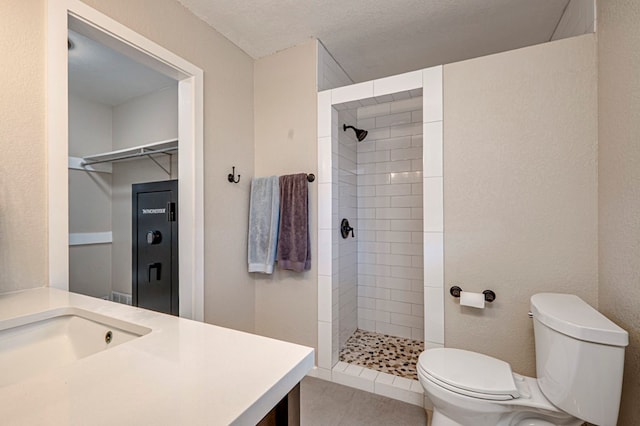 bathroom with vanity, a spacious closet, a tile shower, and toilet