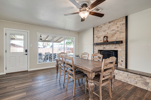 dining room featuring a textured ceiling, a large fireplace, a ceiling fan, dark wood-type flooring, and visible vents