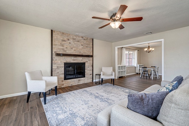 living room with dark wood-type flooring, a textured ceiling, ceiling fan with notable chandelier, and a stone fireplace