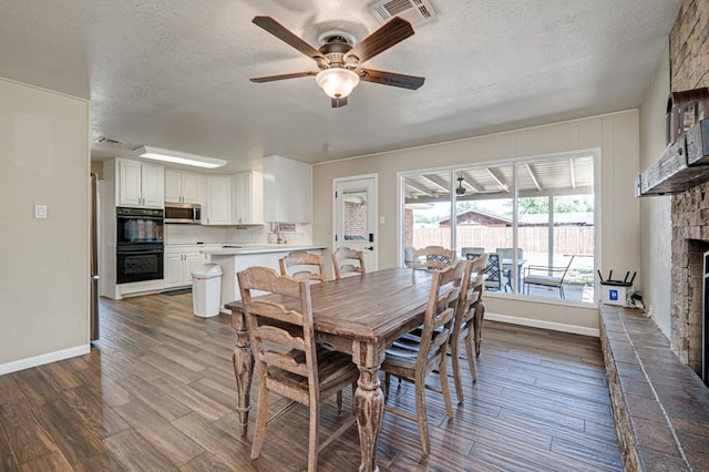 dining space with dark wood-style flooring, a large fireplace, a ceiling fan, baseboards, and visible vents