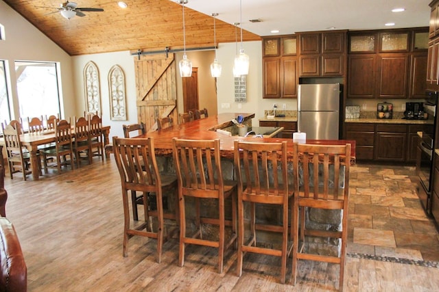 kitchen featuring stainless steel refrigerator, wooden ceiling, a barn door, wood-type flooring, and vaulted ceiling