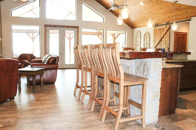 dining room featuring ceiling fan, a barn door, high vaulted ceiling, wood ceiling, and light wood-type flooring