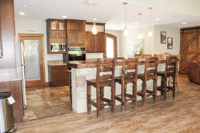 kitchen with appliances with stainless steel finishes, a kitchen breakfast bar, light stone counters, pendant lighting, and a barn door