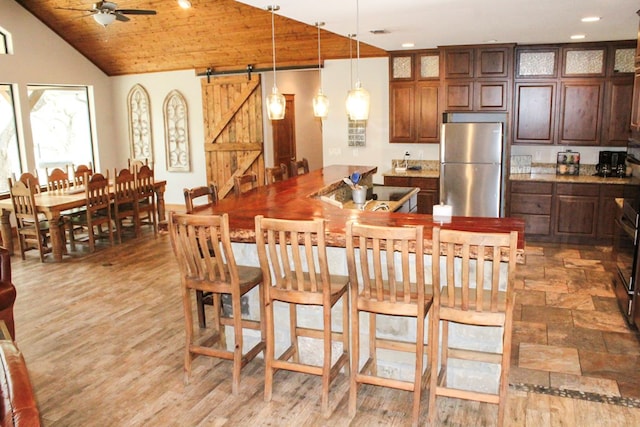 kitchen with stainless steel fridge, wood ceiling, vaulted ceiling, a barn door, and decorative light fixtures