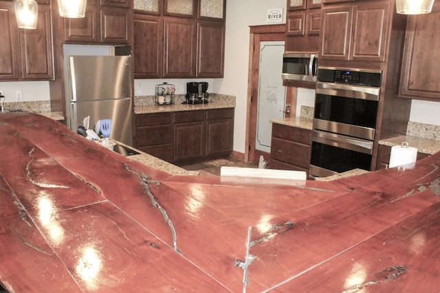 kitchen with stainless steel appliances, light stone counters, hanging light fixtures, and sink