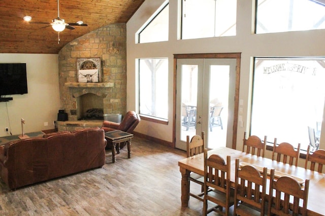 dining space featuring ceiling fan, french doors, wooden ceiling, a stone fireplace, and wood-type flooring