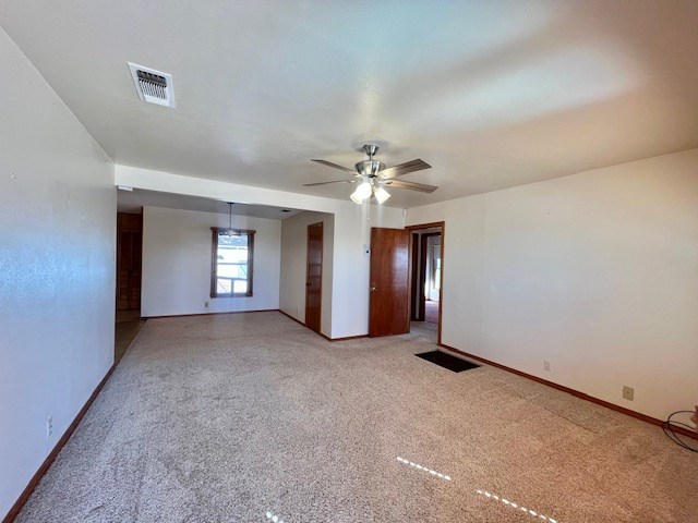 unfurnished room with a ceiling fan, light colored carpet, visible vents, and baseboards