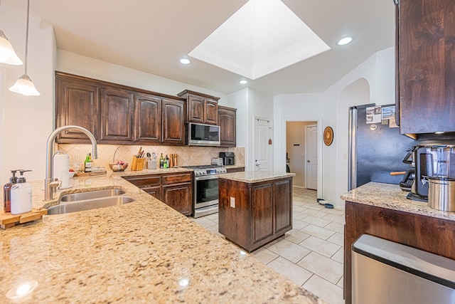 kitchen featuring light stone counters, dark brown cabinetry, a sink, appliances with stainless steel finishes, and decorative backsplash