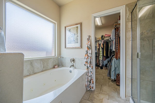 bathroom with a shower stall, a spacious closet, a tub with jets, and stone finish flooring